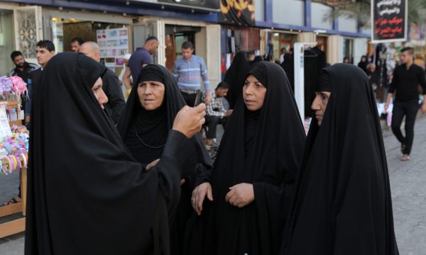 Four women wearing chadors, one checking her phone.