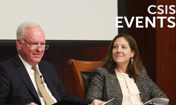 A man in a suit and a woman are seated on a stage during a panel