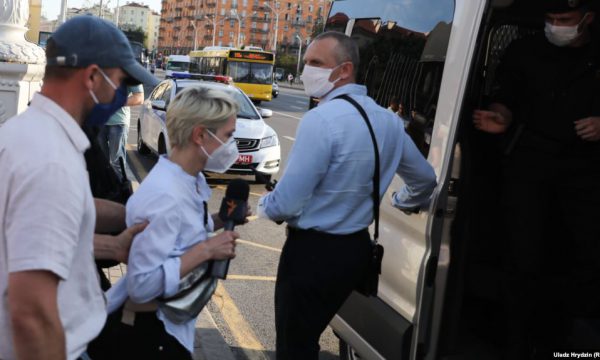 woman with RFERL microphone escorted into van